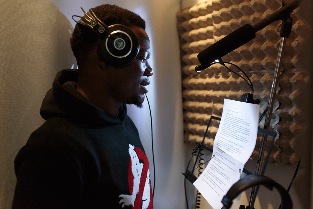 young person with headphones in front of a mic reading a script